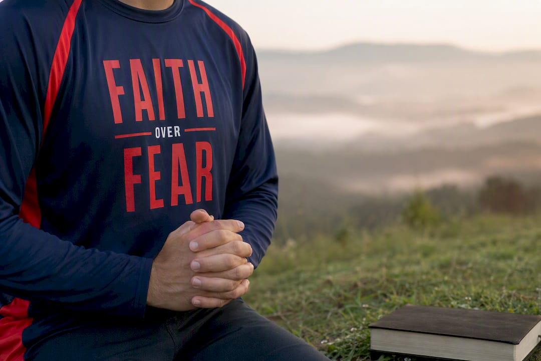 Torso of person wearing Faith Over Fear hoodie with prayer hands